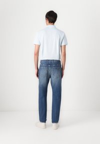 Light blue polo shirt with short sleeves, paired with blue denim jeans. The jeans have a slight fade and five-pocket design, finished with white shoes.