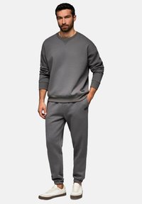 Graues Sweatshirt- und Sweatpants-Set, mit Rundhalsausschnitt und Rippbündchen, aus weichem Stoff. Kombiniert mit weißen Turnschuhen.