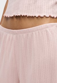Gros plan d'une personne portant un crop top en maille côtelée rose clair et un pantalon taille haute assorti laissant apparaître le ventre.