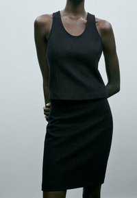 Débardeur noir ajusté et jupe crayon en tissu texturé. Le débardeur présente un col rond, tandis que la jupe arrive à mi-cuisse.