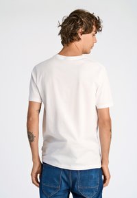 Biała bawełniana koszulka z krótkimi rękawami i okrągłym dekoltem. Charakteryzuje się gładką teksturą i luźnym krojem, noszona z niebieskimi dżinsami.