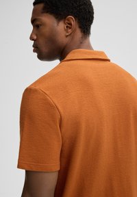 Polo a maniche corte in tessuto ruggine testa di moro, con colletto classico e vestibilità rilassata. Design semplice e moderno.