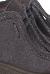 Scarpe in suede grigio con finitura testurizzata. Forma arrotondata, con lacci grigi e dettagli di cucitura. Suola in gomma visibile nella parte inferiore.