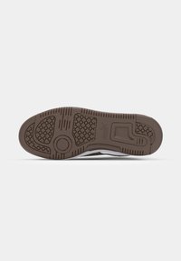 White sneaker sole with brown rubber, featuring circular and hexagonal grip patterns, and a pronounced heel section. Flat and textured surface.