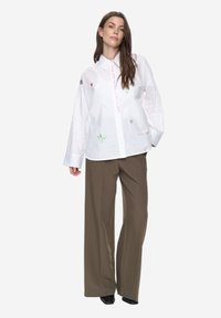 Biała bawełniana koszula z haftem, z kołnierzykiem w szpic, zapięciem na guziki i szerokimi, oversize'owymi rękawami. Połączona z oliwkowozielonymi spodniami o szerokich nogawkach.