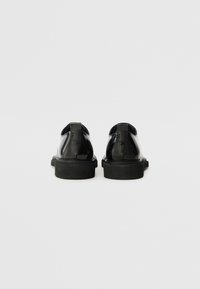 Zwarte lakschoenen met een afgeronde neus, lage hak en een gladde textuur. Ontworpen met een klassieke silhoutte en minimale accenten.