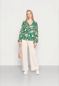 Blusa verde floral de manga longa, com decote em v; calças largas creme; mala rosa; ténis brancos.