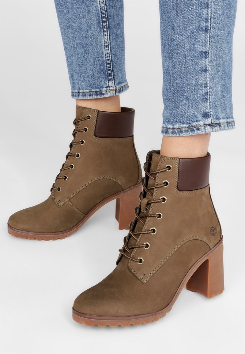 Bottines en daim marron avec un talon épais marron, dotées d'un laçage avant, d'un bout rond et d'un col rembourré. Semelle extérieure en caoutchouc pour une bonne traction.
