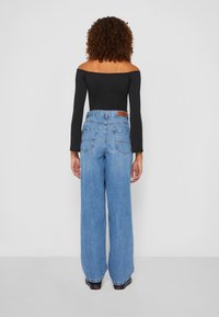 Džíny z džínoviny s vysokým pasem a širokými nohavicemi v světle modré barvě s mírně vybledlým efektem, s dvěma zadními kapsami a hnědou koženou štítkem v pase.