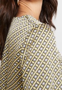 Musterbluse mit einem geometrischen Design aus Sechsecken in Weiß, Schwarz und Grüntönen, aus einem weichen, strukturierten Stoff und in lässigem Schnitt.