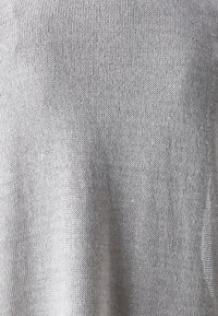 Ljusgrått, stickat tyg med en mjuk, texturerad yta; har en lös, öppen väv som skapar en andningsbar design.