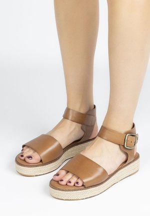 Brown leather sandals with wide straps and buckle detail; elevated cork platform sole with woven texture; open-toe design.