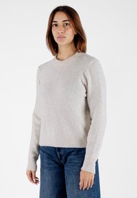 Maglione beige chiaro realizzato in tessuto a maglia testurizzato. Collo rotondo e polsini a coste. Abbinato a jeans di denim blu.