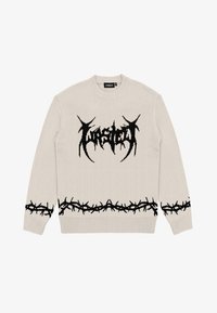 Ljusbeige stickad tröja med svart abstrakt logotyp på bröstet och taggtrådsmönster längs fållen och ärmarna.