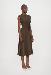 Rochie maro fără mâneci, cu un corset ajustat și fusta evazată, realizată dintr-un material neted. Detaliu remarcabil cu cusătură unghiulară la talie.