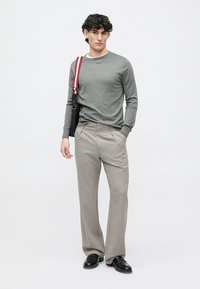 Siva majica z dolgimi rokavi, bež kravate hlače, črne čevlje in torba z rdečim in črnim trakom, na belem ozadju.