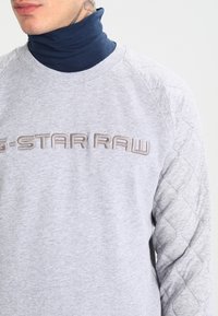 Felpa grigia con maniche a motivo trapuntato e collo a maglia. Presenta un ricamo in rilievo "G-STAR RAW" di colore marrone chiaro sul davanti.
