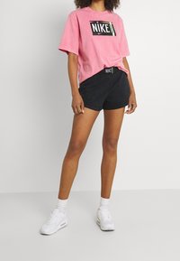 Rosa bomull t-shirt med svart Nike-logotyp, matchad med svarta bomullsshorts med elastisk midja och Nike-märke. Vita sneakers fulländar looken.