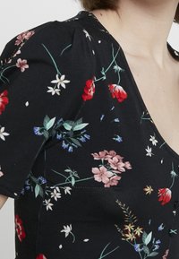 Halenka s květinovým vzorem na černém pozadí, s krátkými nabíranými rukávy, výstřihem do V a různými květinami v červené, růžové a bílé barvě.