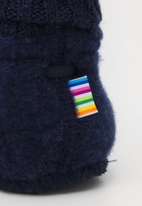 Calcetín de lana de punto azul marino con un cuerpo texturizado y una etiqueta a rayas multicolores cosida en el lado. Punta redondeada y detalles de costura en las costuras.