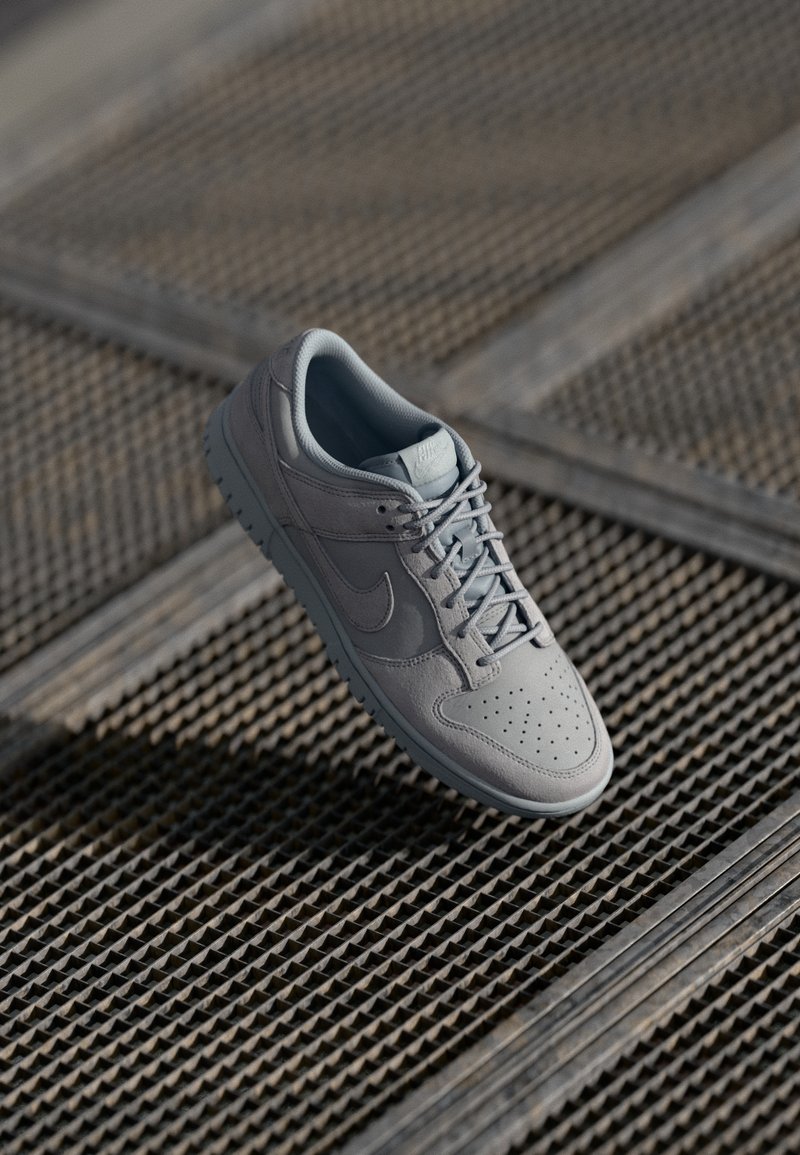 Grey leather sneaker with perforated toe, laces, and a rubber sole. Designed with a subtle swoosh logo and a smooth finish.