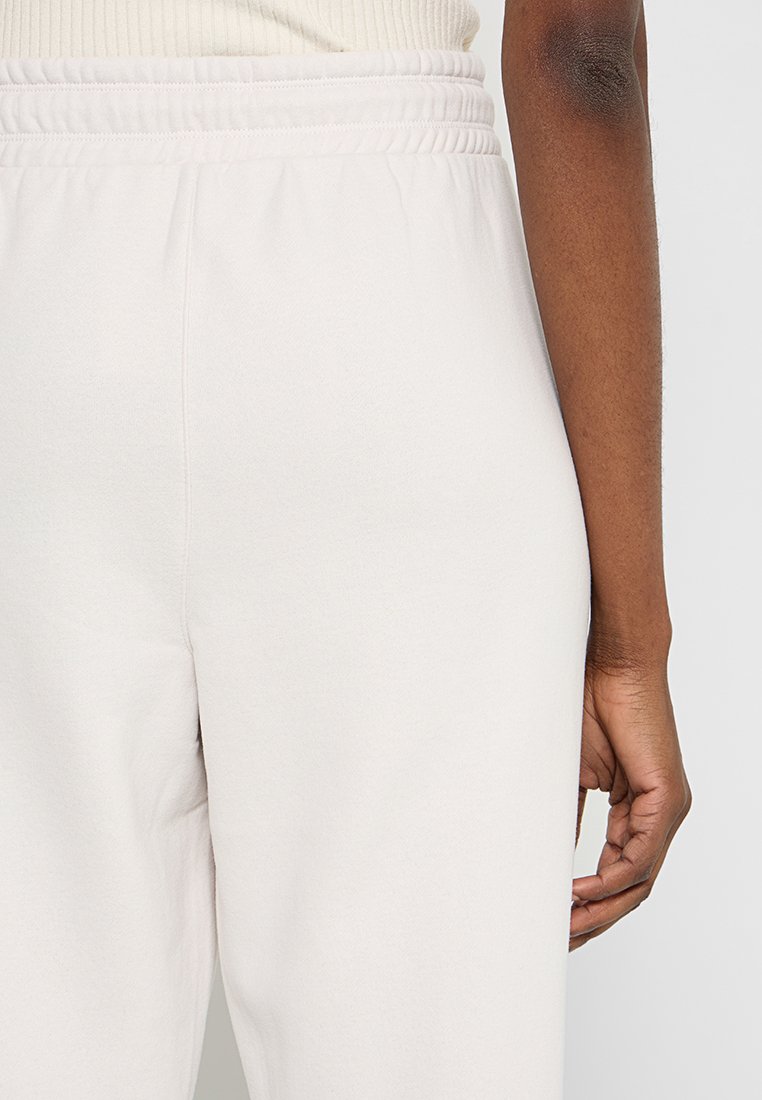 Jasno beżowe dresy z elastycznym pasem. Materiał wydaje się miękki i gładki, z luźnym krojem i bez widocznych hardware'ów oraz kieszeni.