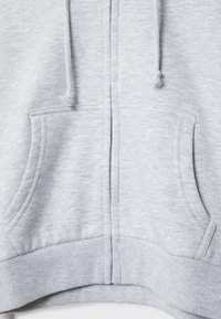 Sweat à capuche gris clair zippé à l'avant avec deux poches pour les mains, des cordons et une taille côtelée dans une texture de tissu doux.