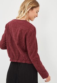 Chaqueta corta burdeos hecha de un tejido texturizado con un patrón floral, que cuenta con mangas largas y un dobladillo elástico para un ajuste ceñido.