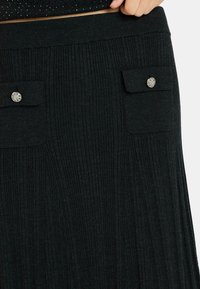Gonna nera a coste con una texture lavorata a maglia e due tasche a ribalta con bottoni metallici. Vita elastica per comfort e facilità di indossarla.
