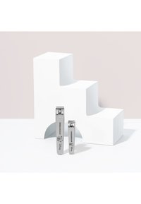 Deux coupe-ongles en acier inoxydable de tailles différentes sont posés près d'une structure d'exposition géométrique blanche aux bords arrondis.