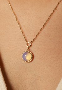 Gouden ketting met een ronde hanger met een doorzichtige paarse en gele steen, die een gladde textuur en glanzende afwerking toont.