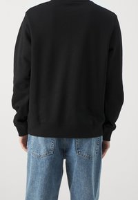 Svart bomullströja med långa ärmar, ribbade muddar och nederkant, stylad med ljusblåjeans, som visar en avslappnad passform och enkel design.