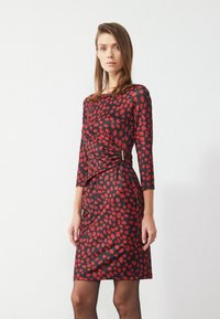 Rotes und schwarzes Polka-Dot-Kleid mit langen Ärmeln, figurbetontem Schnitt, gerafftem Seitendetail und einer eleganten, glatten Textur.