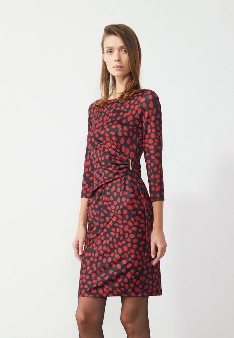 Rotes und schwarzes Polka-Dot-Kleid mit langen Ärmeln, figurbetontem Schnitt, gerafftem Seitendetail und einer eleganten, glatten Textur.