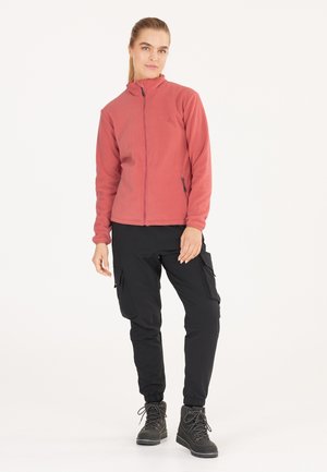 Fleecejacka i korall med hög krage och framsida dragkedja, kombinerad med stretchiga svarta cargo-byxor med flera fickor och smalnade ände.