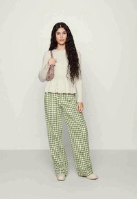 Světlý béžový peplum svetr z texturovaného materiálu, zkombinovaný s širokými kalhotami v zeleném houndstooth vzoru. Neutrální slip-on boty a růžová kabelka.