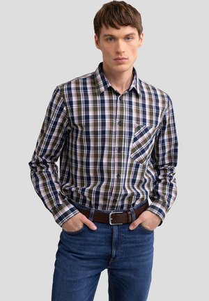 Camisa de cuadros de manga larga en tonos azul marino, verde y blanco, con cuello abotonado y bolsillo frontal. Combinada con jeans azules y un cinturón marrón.