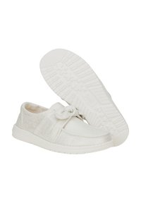 Baskets en toile blanches avec une finition texturée, présentant un nœud noué à l'avant et une semelle en caoutchouc blanche avec un motif de crampons.
