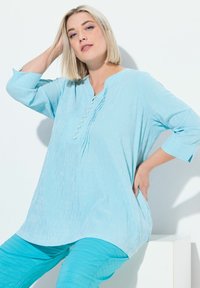 Lichtblauwe tuniek met verticale strepen, 3/4 mouwen, knoopsluiting en een losse pasvorm, gecombineerd met bijpassende turkooise broek.