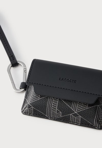 Малък черен калъф за карти Lacoste с геометричен модел, прикрепен към черен ремък със сребърен карабинер.