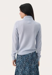 Light blue, knitted sweater with a high collar and ribbed cuffs, worn over a dark floral-patterned skirt. Soft texture and fitted design.