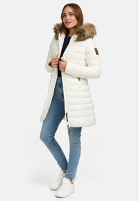 White puffer coat with a fur-lined hood, featuring a zip closure and side pockets. Paired with blue jeans and white sneakers.