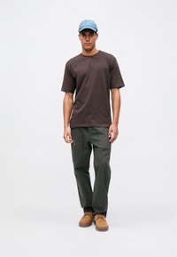 Brun kortärmad skjorta, olivgröna cargobyxor, beige skor och en ljusblå keps. Enkelt mönster med avslappnad passform och enhetliga färger.