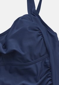 Marinblå baddräktstopp med rynkad textil, justerbara axelremmar, slät yta och ett förstärkt band under bysten för stöd.