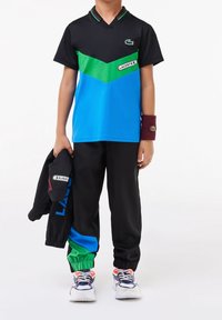 Black short-sleeve polo with green and blue chevron design, paired with black track pants featuring green and blue accents, and sneakers.