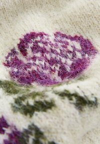 Tessuto lavorato a maglia con un dettagliato motivo floreale viola e bianco e foglie verdi su uno sfondo avorio morbido.