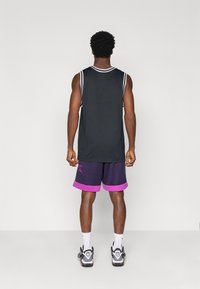 Μαύρο αμάνικο μπλουζάκι με λευκή επένδυση, σε συνδυασμό με μοβ βερμούδα με ροζ λεπτομέρειες. Φοριέται με λευκές κάλτσες και μαύρα αθλητικά παπούτσια.