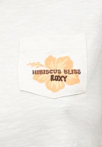 Λευκή υφασμάτινη τσέπη με κίτρινο άνθος ιβίσκου και το κείμενο «HIBISCUS BLISS ROXY» κεντημένο με καφέ χρώμα στο μπροστινό μέρος.