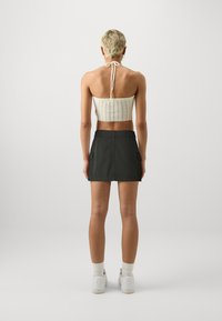 Crop top bianco all'uncinetto con legacci al collo, abbinato a una mini gonna verde scuro con tasche; modella di spalle. Sneakers bianche e calzini alti.