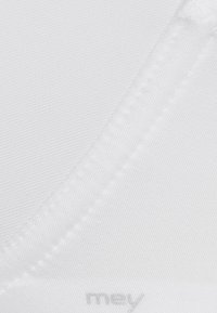 White seamless bra with a smooth texture, featuring thin straps and flat seams, brand name subtly printed near the bottom.
